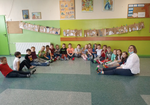 Zdjęcie grupowe klasy 1a. Uczniowie siedzą na podłodze i pokazują swoje kolorowe skarpetki.